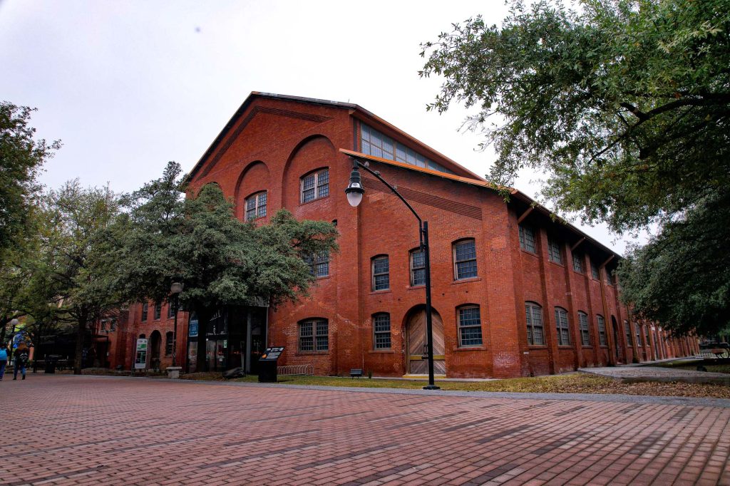 Nave industrial de ladrillo rojo rehabilitada, con ventanas de arco y explanada de adoquÃ­n entre Ã¡rboles.