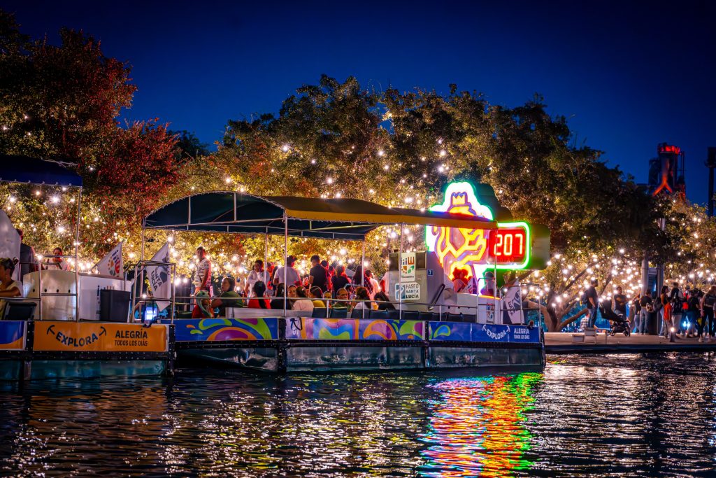 Barco turÃ­stico del Paseo Santa LucÃ­a lleno de visitantes junto a un letrero de neÃ³n por la noche