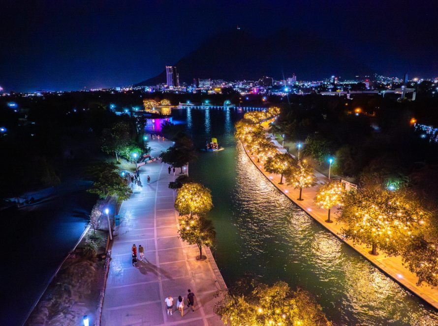 Vista nocturna del canal del Paseo Santa LucÃ­a con barco turÃ­stico, Ã¡rboles iluminados y la ciudad al fondo.